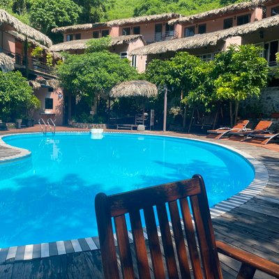 Ghế gỗ bên hồ bơi và dãy bungalow mái lá tại Cat Ba Oasis.