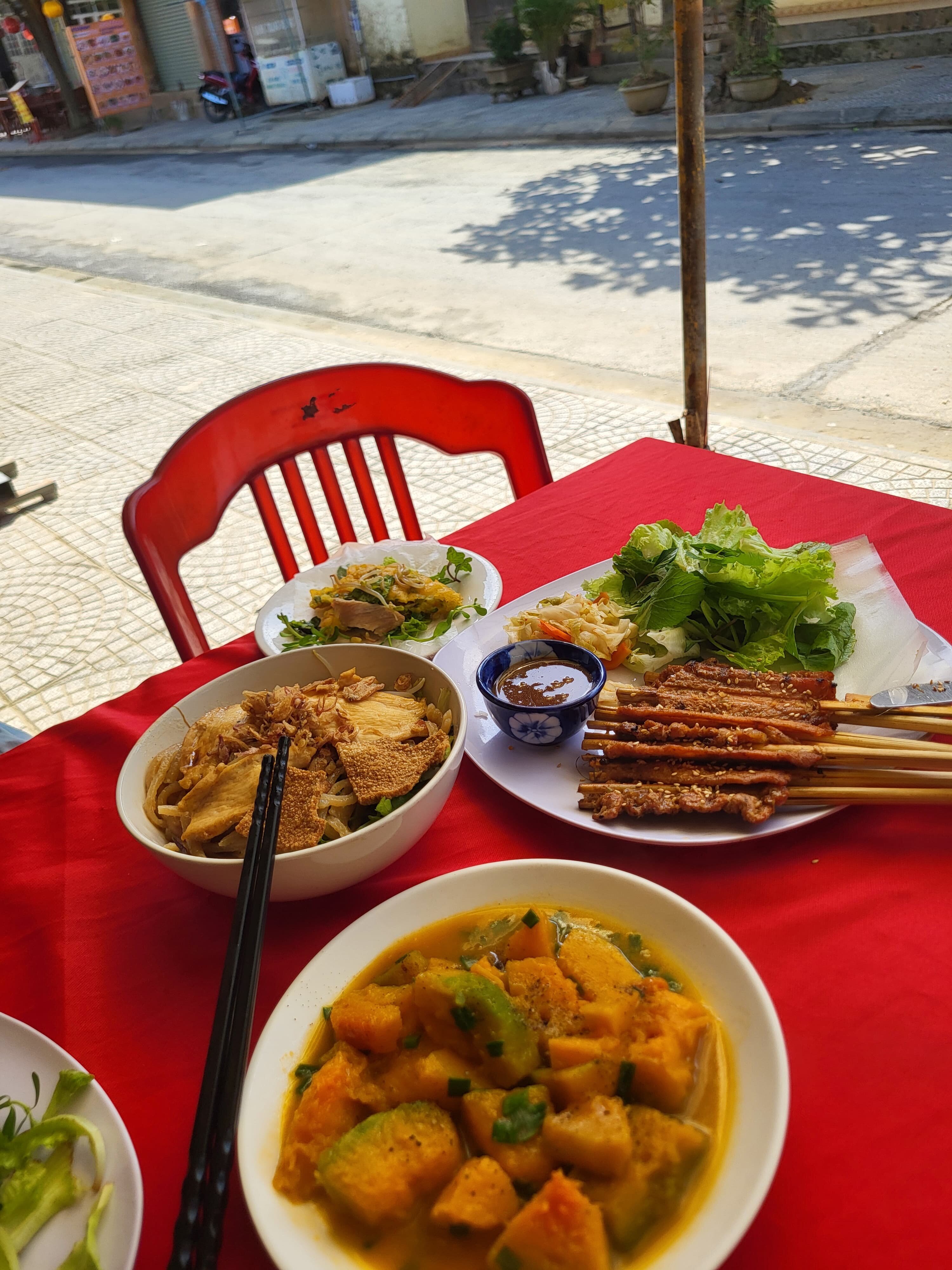 Cao lầu, thịt xiên nướng cuốn bánh tráng và bát bí đỏ trên bàn sát vỉa hè ở Hi Restaurant.