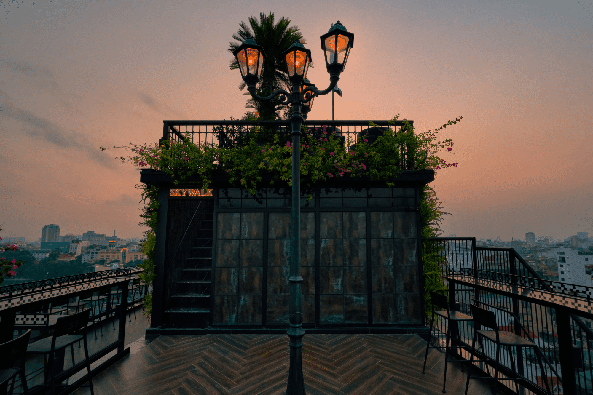 Khối Skywalk phủ hoa giấy và cột đèn cổ trên sân thượng Lighthouse Sky Bar lúc hoàng hôn.