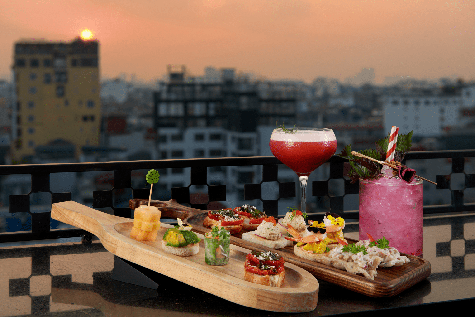 Đĩa canapé và hai ly cocktail bên lan can sân thượng Lighthouse Sky Bar.