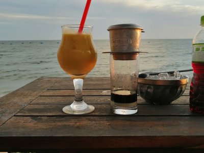 Ly sinh tố và cà phê phin trên bàn gỗ nhìn ra biển tại Lọ Lem Cafe