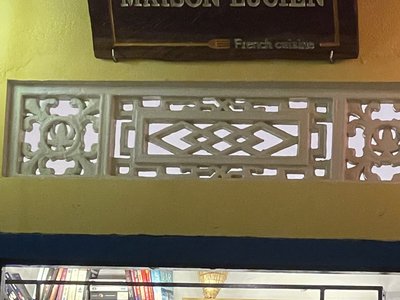 Bảng tên Maison Lucien và ô gió hoa văn trên tường vàng