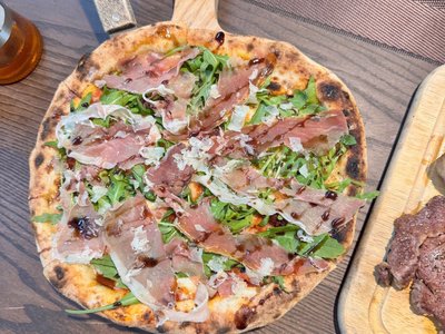 Pizza đế mỏng phủ thịt nguội, rau rocket và phô mai bào trên khay gỗ tại Pizza Goong