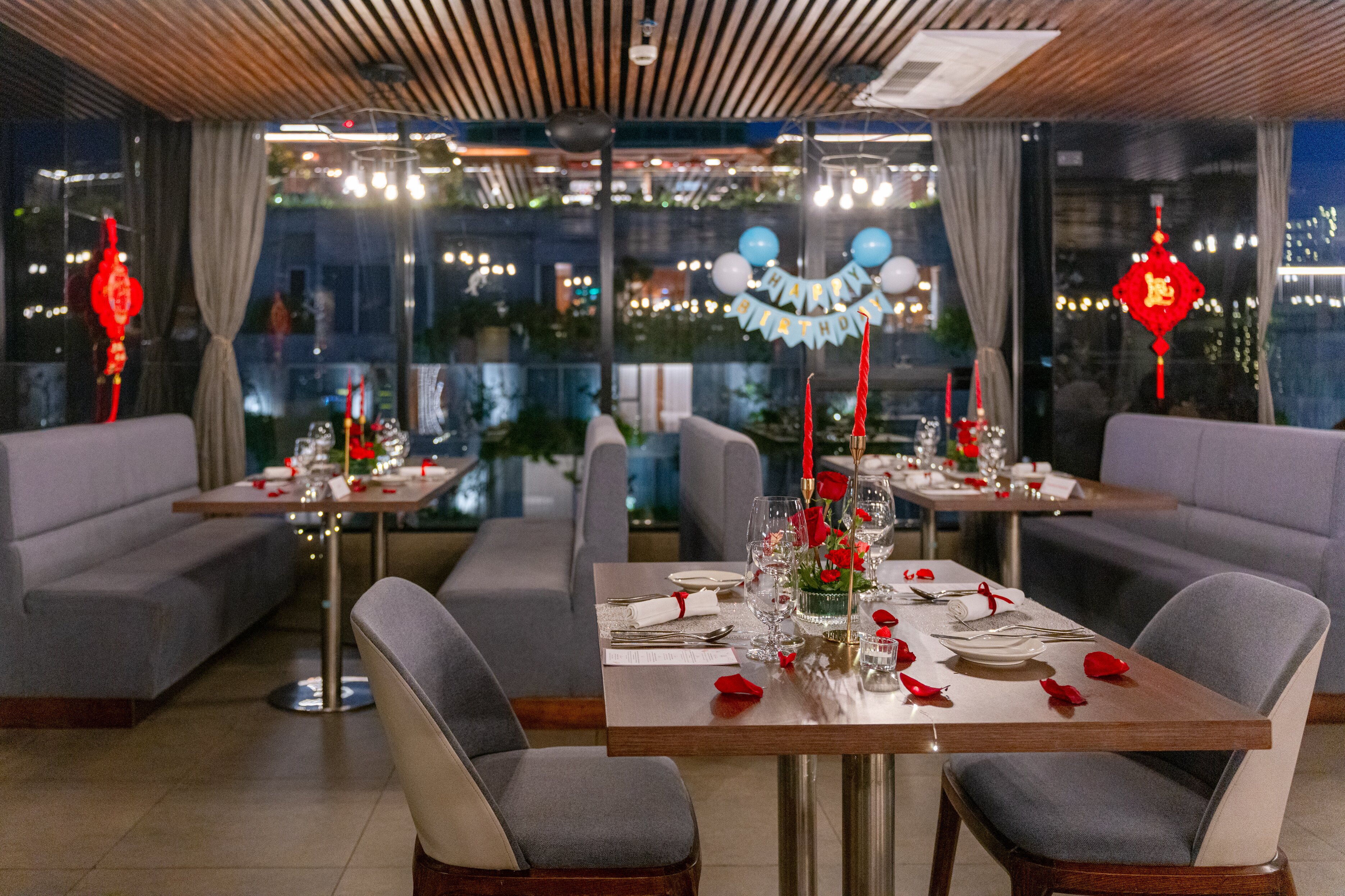 Bàn ăn bày hoa hồng, nến đỏ và băng rôn sinh nhật bên vách kính tại Sky View Restaurant