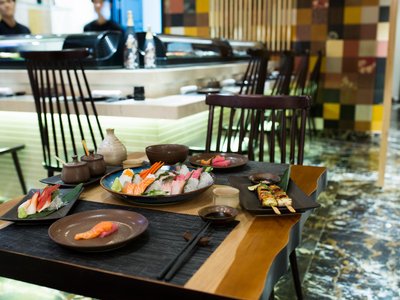 Khay sashimi, xiên nướng và đĩa cá hồi trên bàn gỗ gần quầy sushi của WaKaKu, Hội An