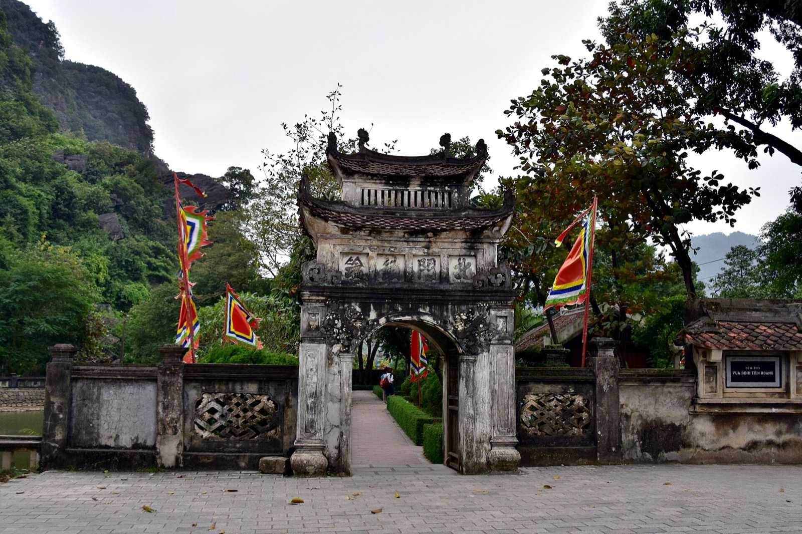 Cổng đá rêu phong có cờ hội hai bên trong khu di tích Cố đô Hoa Lư, phía sau là núi đá